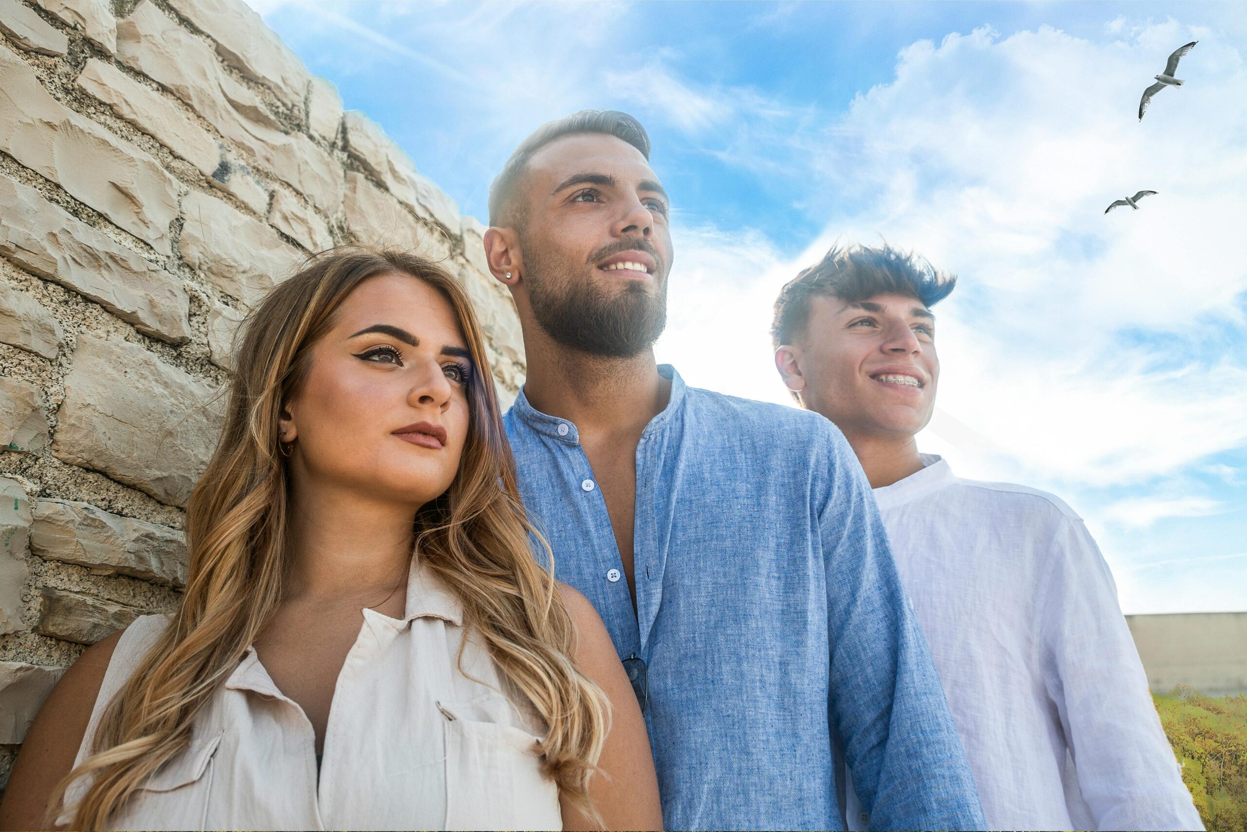 Three friends smiling outdoors on a summer day with clear blue skies.