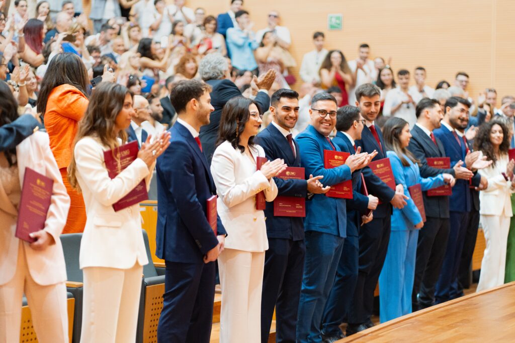 A diverse group of graduates celebrate their achievement in a lively indoor ceremony, showcasing excitement and joy.