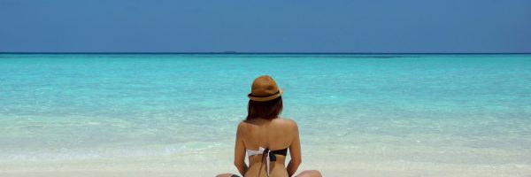 Rear view of a woman in a bikini and hat relaxing on a pristine beach in Maldives.